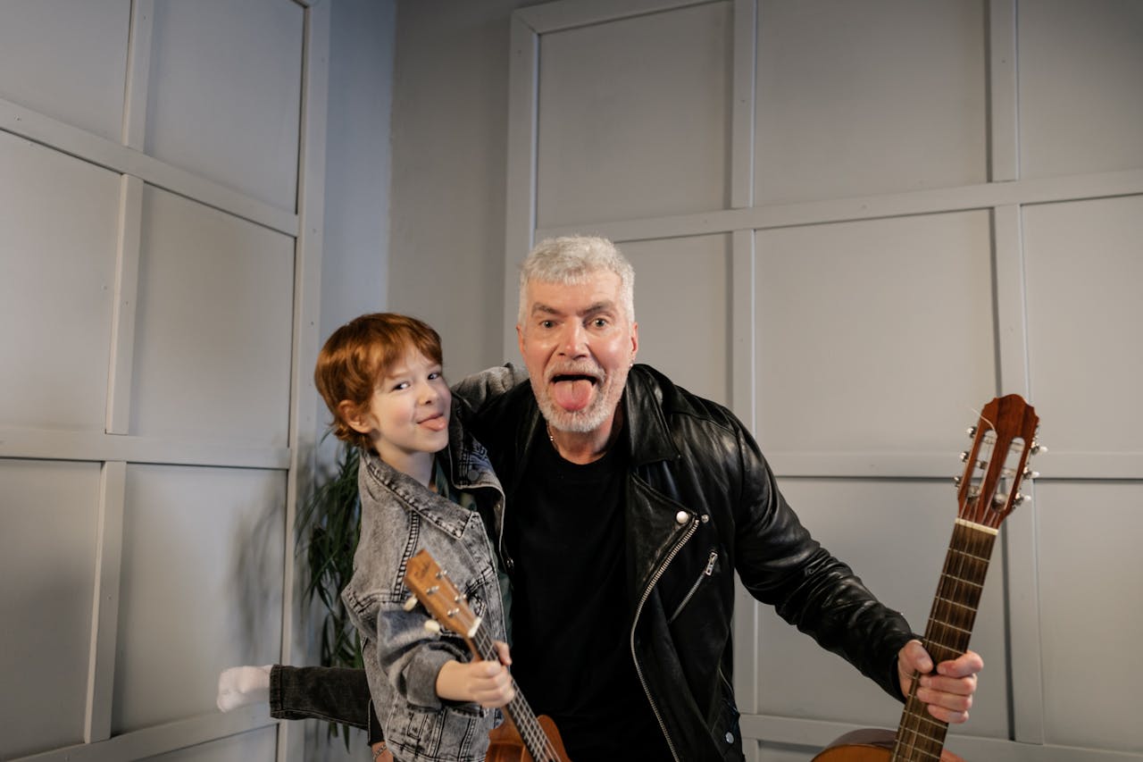 A cheerful grandfather and grandson share a fun moment playing guitars indoors.