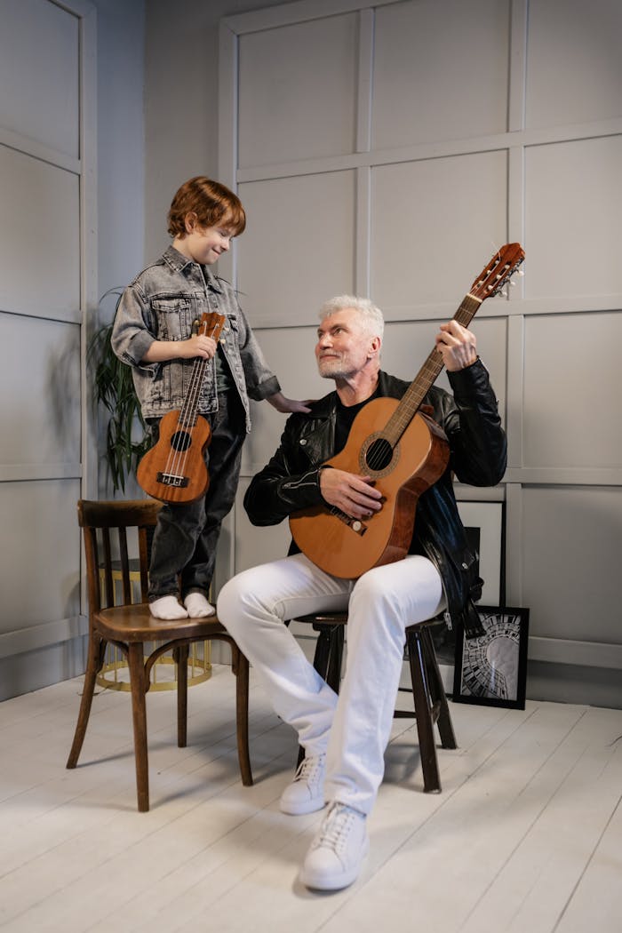 A grandfather and grandson enjoying music together playing guitars indoors.